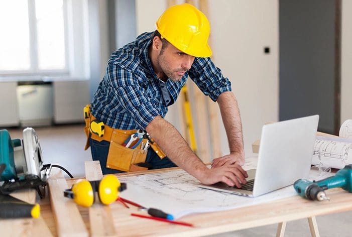 A man in yellow hard hat using laptop on table.