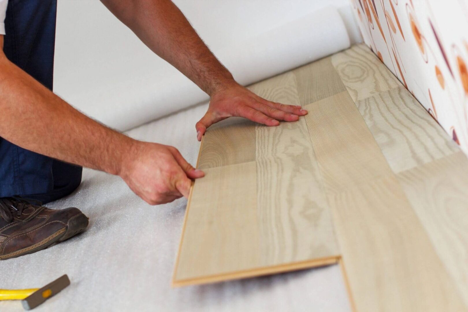 A person is laying down some wood flooring